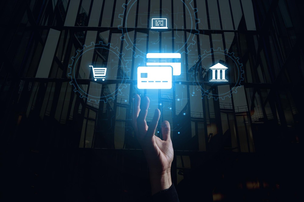 A hologram depicting debit and credit cards surrounded by icons of a shopping cart, a bank, and a computer while a hand reaches out for them