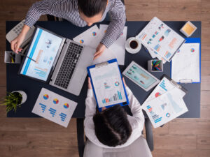 Two people in a meeting using a laptop and looking at several graphs